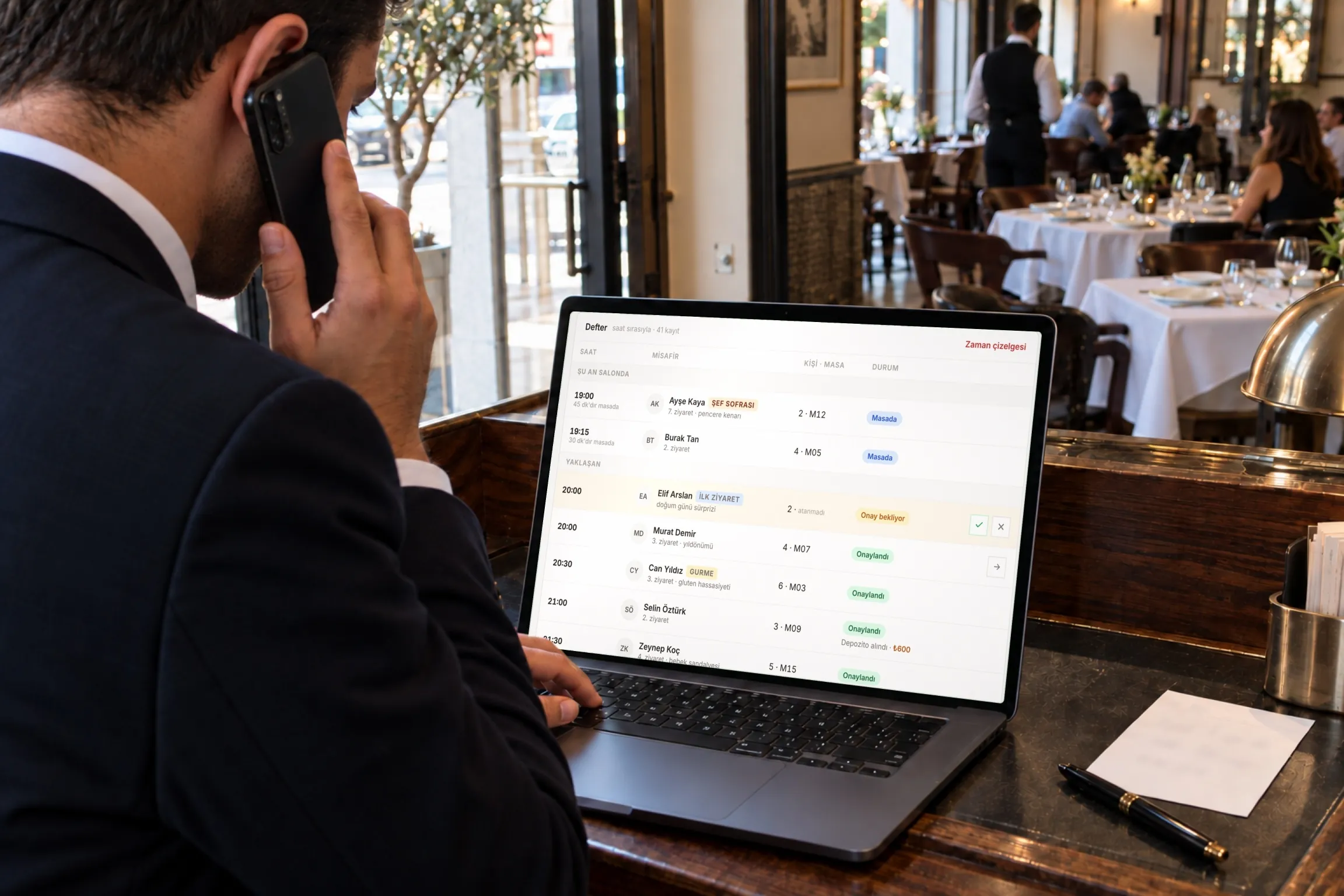 Kürsüde telefonla rezervasyon alırken dizüstünde DineLuup defterine bakan müdür